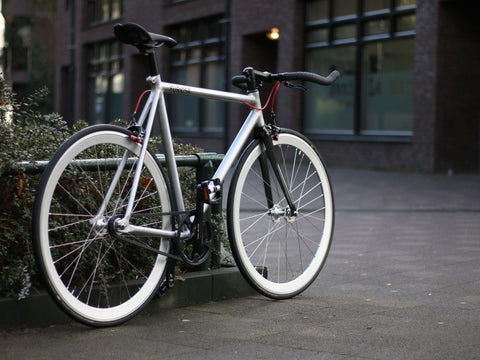 Silbernes Singlespeed-Rad an einem Geländer, die roten Bremszughüllen laufen am Rahmen entlang