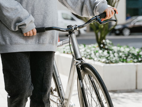 Person schiebt ein Fahrrad über den Gehweg, die Hand liegt am Bremshebel des geraden Lenkers