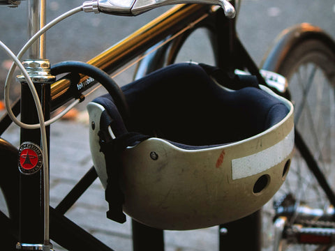 Stark abgenutzter heller Fahrradhelm mit Kratzern und ausgeblichener Schale hängt am Rahmen eines goldfarbenen Stadtrads