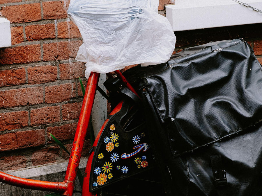 Sattel eines roten Stadtrads mit einer Plastiktüte vor Regen geschützt, daneben eine schwarze Gepäckträgertasche